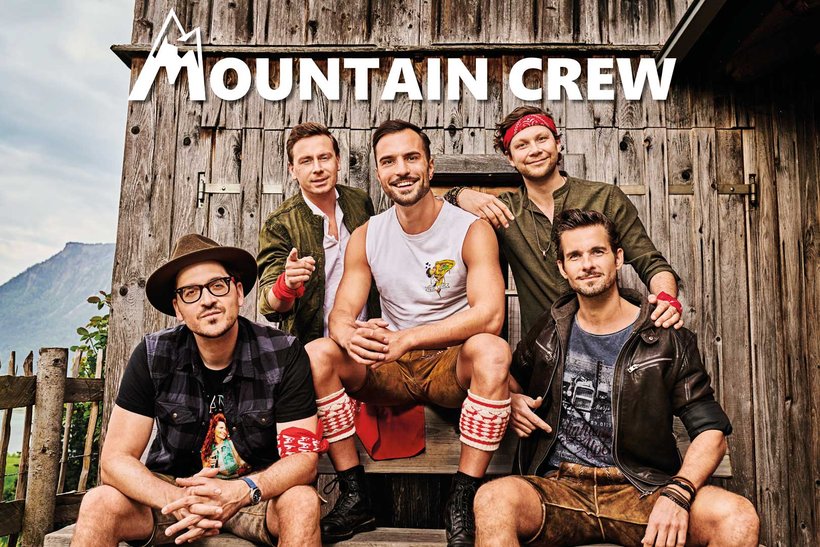 Die Band Mountaincrew (5 Burschen im Lederhosenoutfit) sitzt vor einer Holzhütte